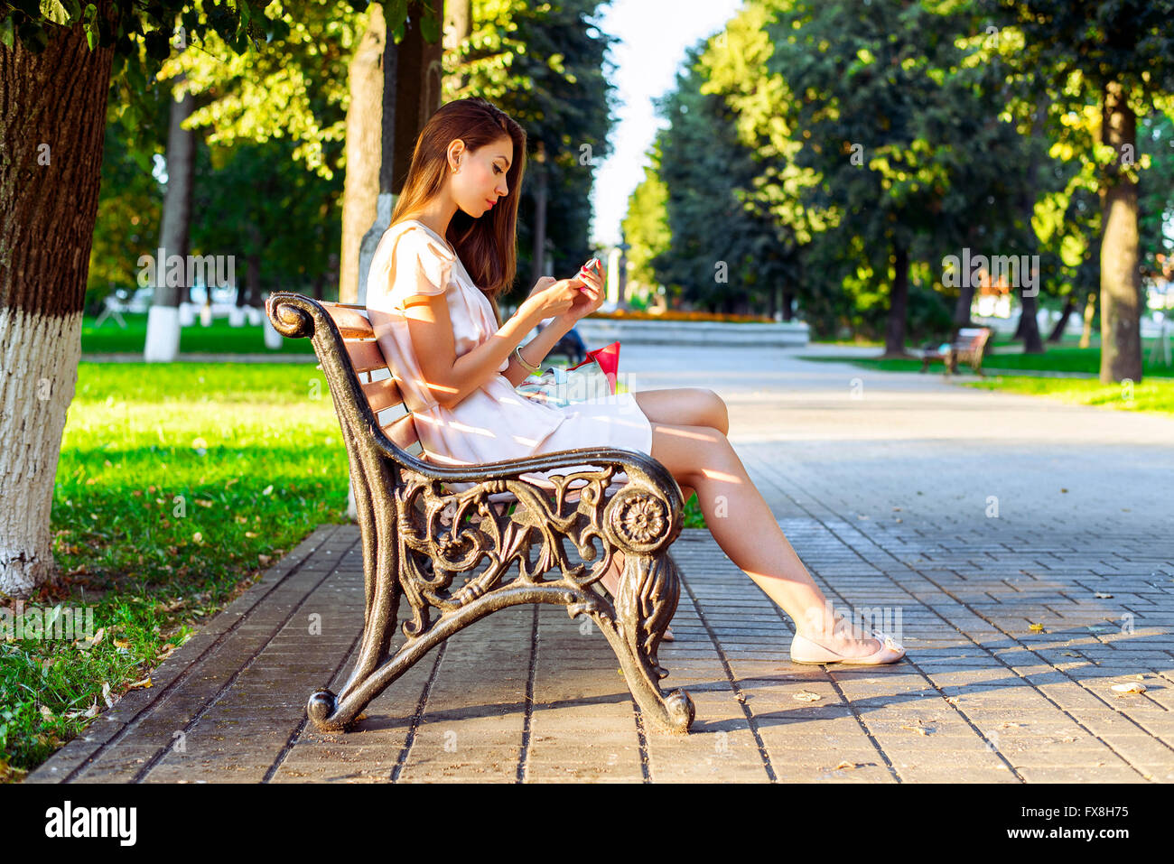 Beautiful Girl sitting bench, brunette robe rose, la mode style de vie avec votre téléphone enregistre un message sur les réseaux sociaux Banque D'Images
