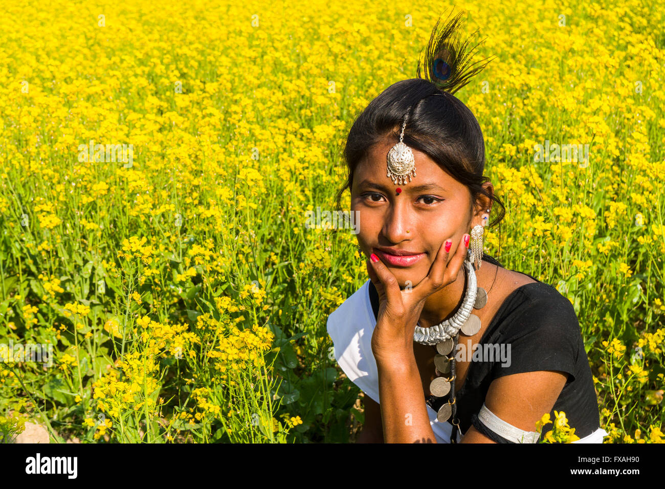 Portrait d'une jeune femme appartenant à la tribu Tharu, assis dans un champ de moutarde jaune, Chitwan, Chitwan, Népal Banque D'Images