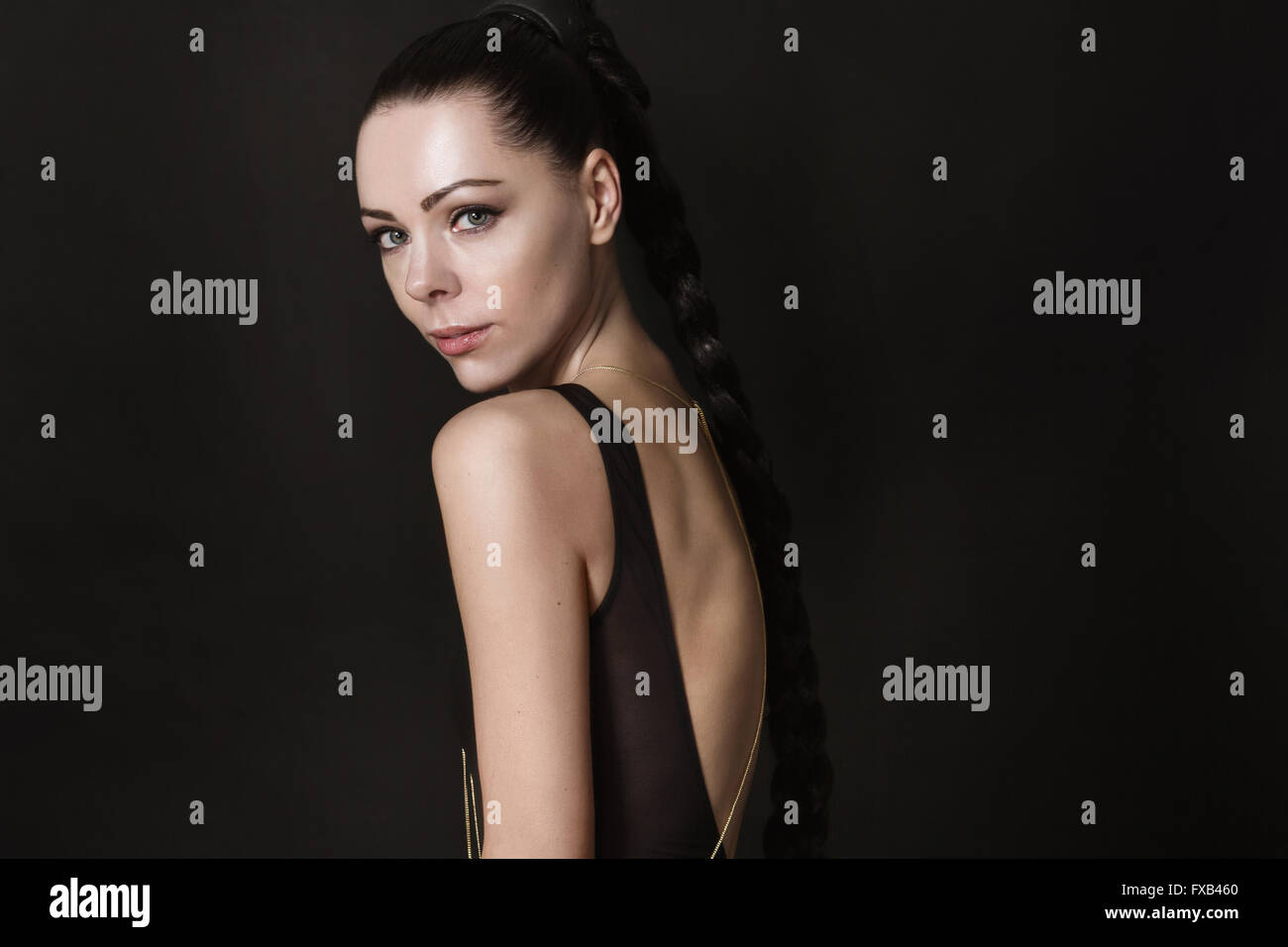 Portrait d'une jolie jeune femme en vêtement de cuir noir. Elle se tient en un demi-tour. Son dos est ouvert. Il est considéré un Banque D'Images