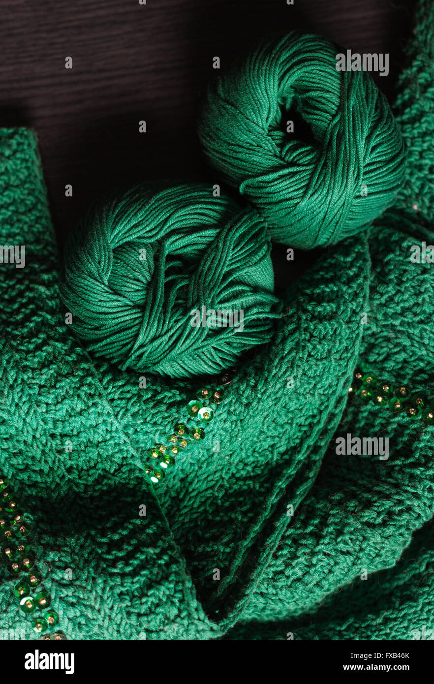 Deux balles de laine vert et vert foulard perlé établit sur une table en bois sombre. Le fil est d'un vert profond. Perles sont l'or et brillants. Banque D'Images
