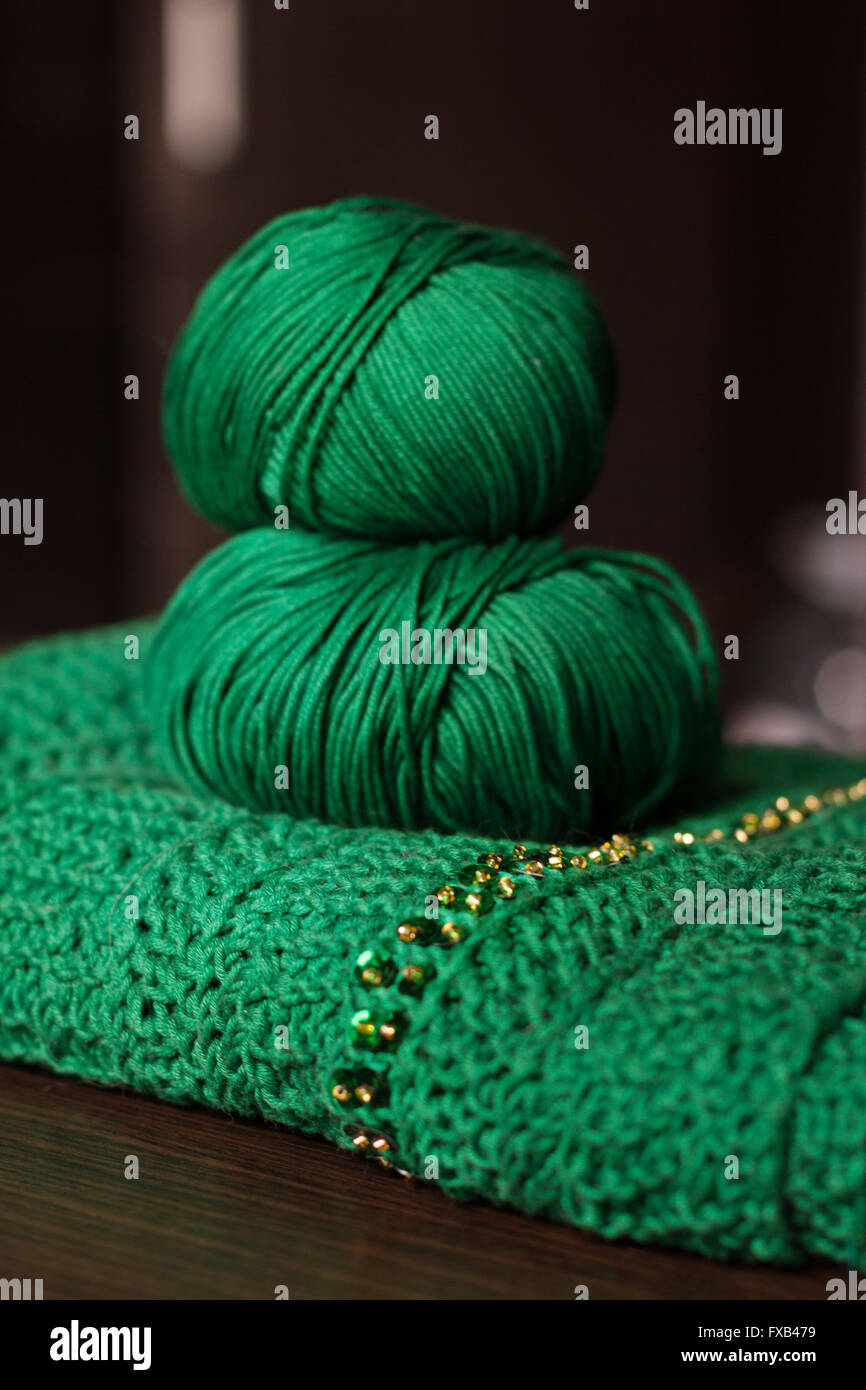 Deux balles de laine vert et vert foulard perlé établit sur une table en bois sombre. Le fil est d'un vert profond. Perles sont l'or et brillants. Banque D'Images