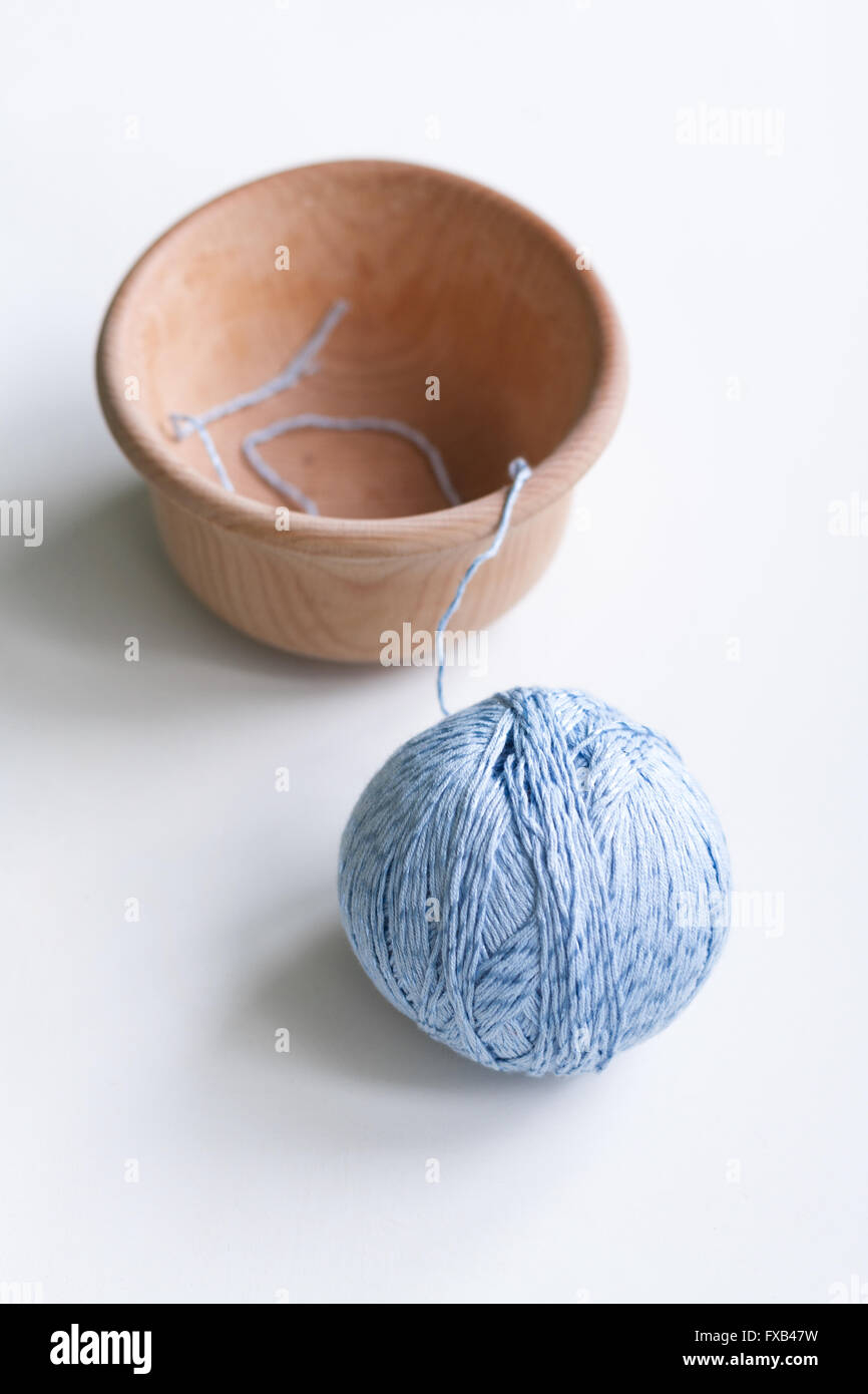 Pelote de laine bleu unique se trouve sur un tableau blanc à côté d'un bol en bois. Banque D'Images