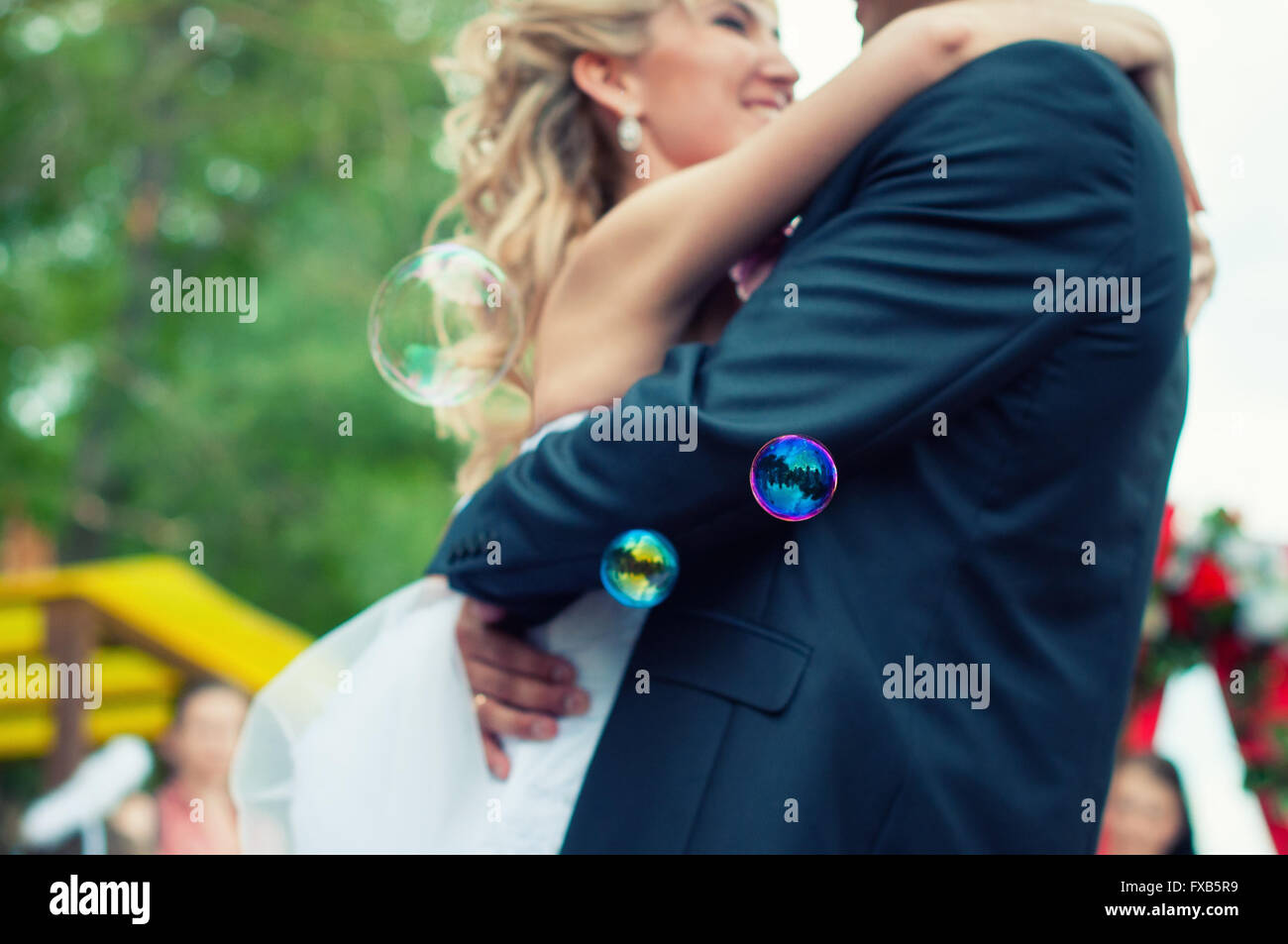 Mariée et le marié sont marcher ensemble dans un parc. Ils s'embrassent. Couple est floue et les bulles de savon sont le vol de foreg Banque D'Images Mariée et le marié sont marcher ensemble dans un parc. Ils s'embrassent. Couple est floue et les bulles de savon sont le vol de foreg Banque D'Images