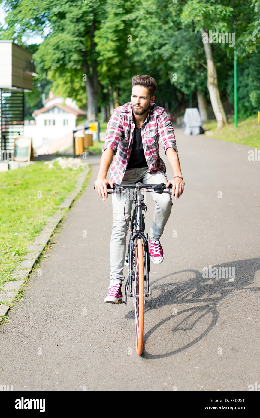 Beau jeune homme aux yeux bleus sur son vélo dans une allée d'arbres , regardant la caméra et enjoyng printemps Banque D'Images