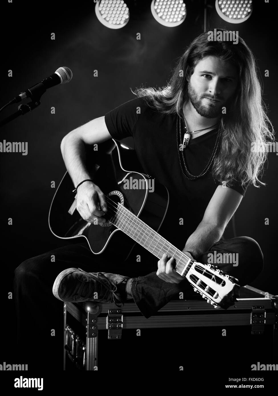 Photo d'un jeune homme aux cheveux longs et une barbe jouant une guitare acoustique sur scène avec des lumières et les concerts atmosphère. Banque D'Images
