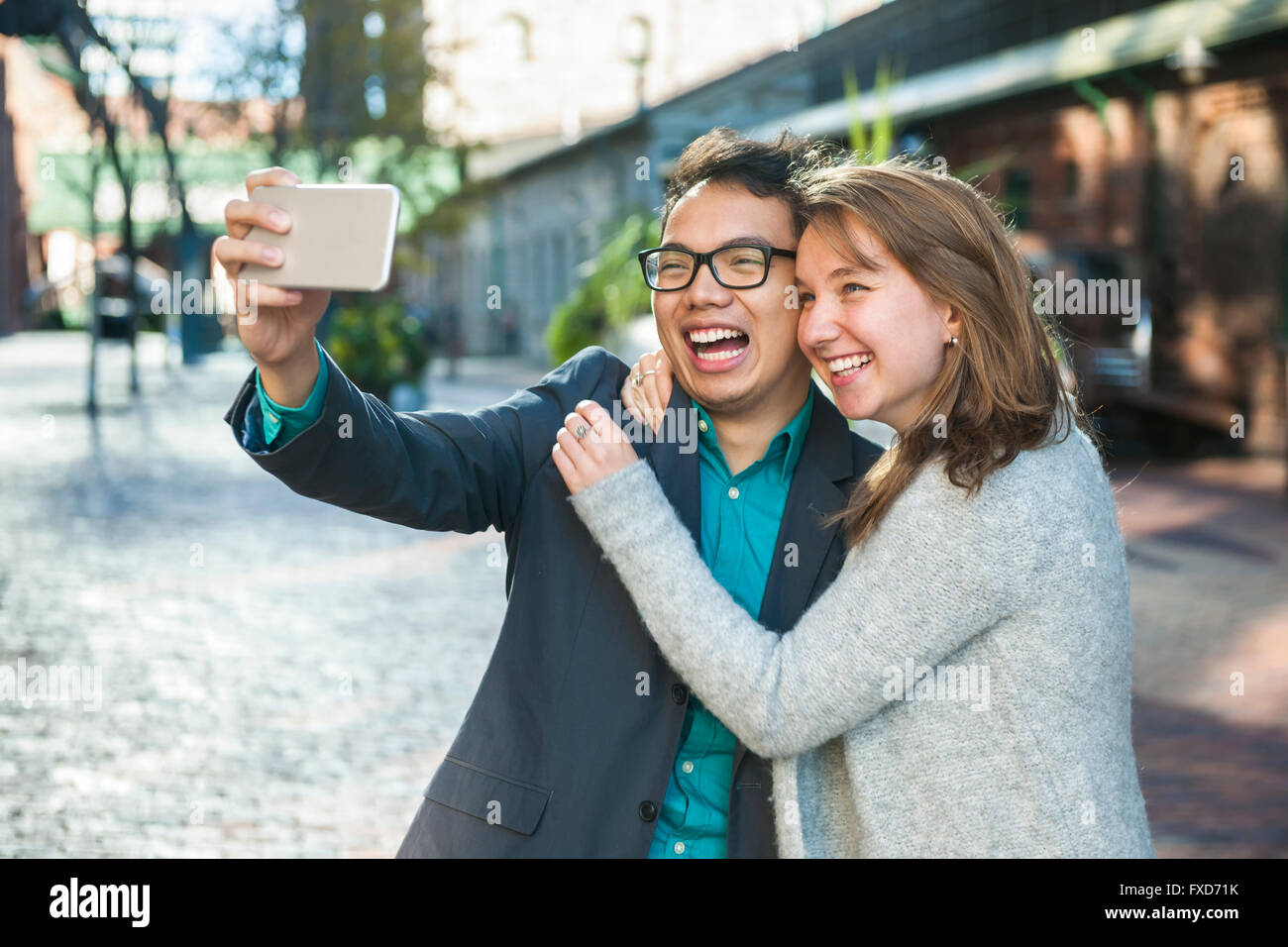 Deux jeunes gens rire prenant un appareil mobile avec selfies en dehors on city street Banque D'Images