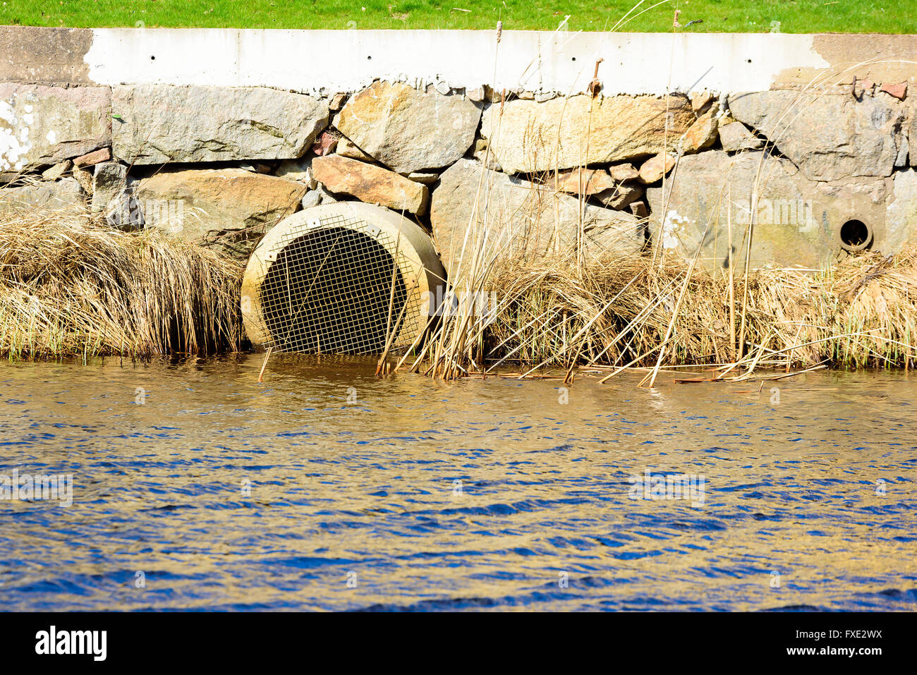 Déduits d'eaux pluviales en sortie d'une rivière avec des blocs de pierre et d'une partie d'une pelouse au-dessus. Banque D'Images