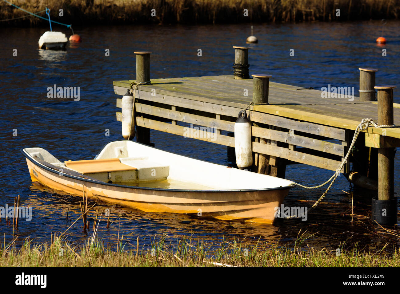 Barque en plastique orange rempli d'eau amarré à une jetée en bois au printemps. Banque D'Images
