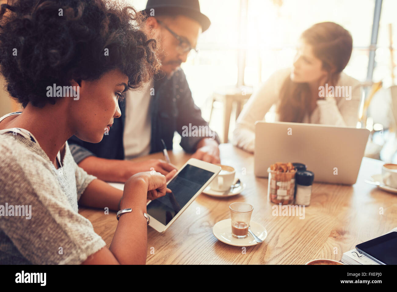 Close up portrait of young woman using digital tablet avec ses amis assis à une table de café. Groupe de jeunes Banque D'Images