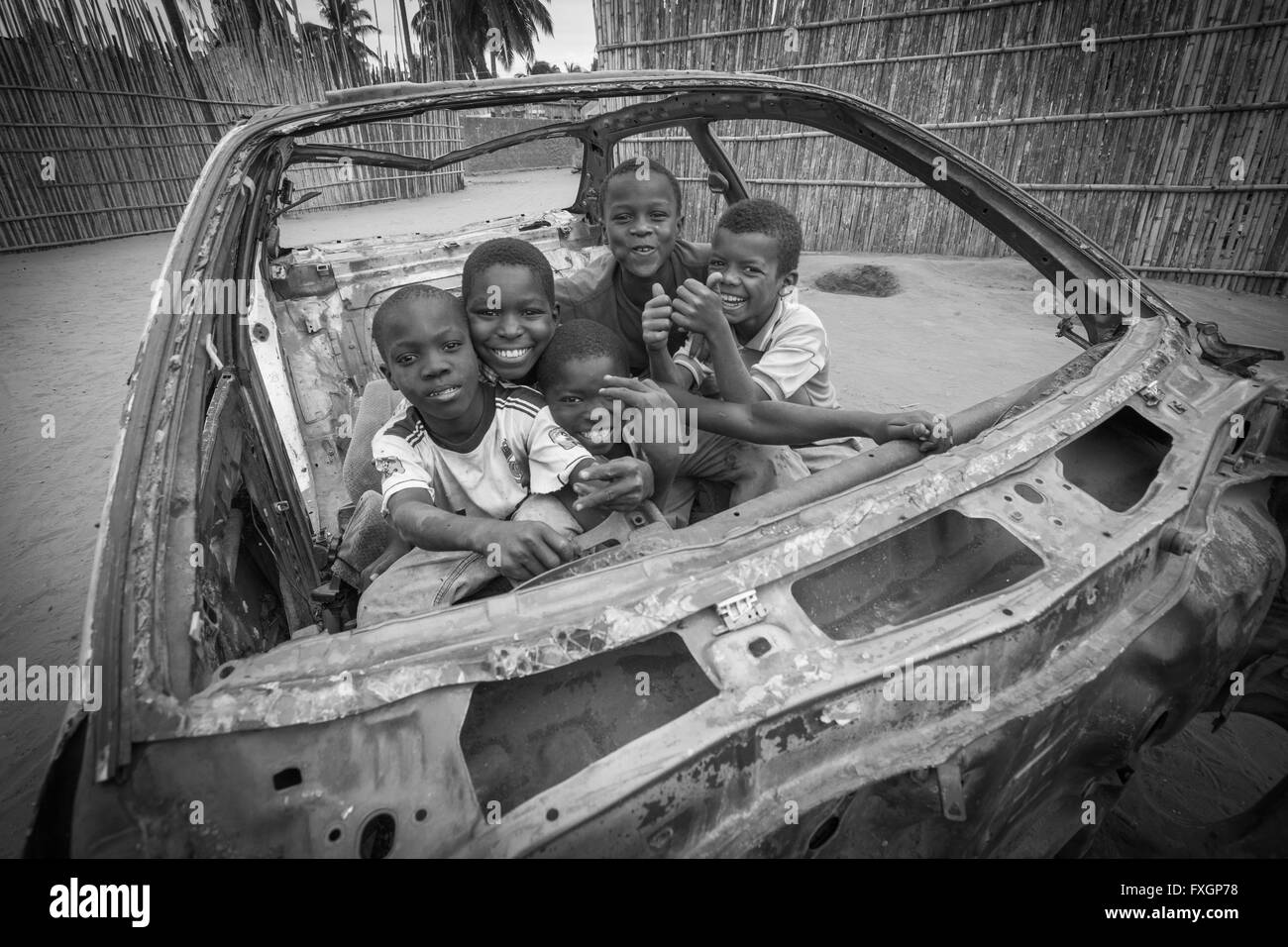 Le Mozambique, heureux enfants jouant dans une voiture endommagée, noir et blanc. Banque D'Images