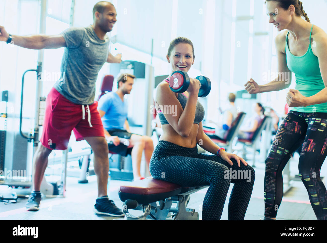 Woman cheering sur ami faisant haltère biceps at gym Banque D'Images
