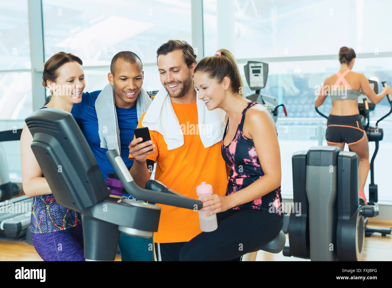 Smiling friends using cell phone at exercise bike in gym Banque D'Images