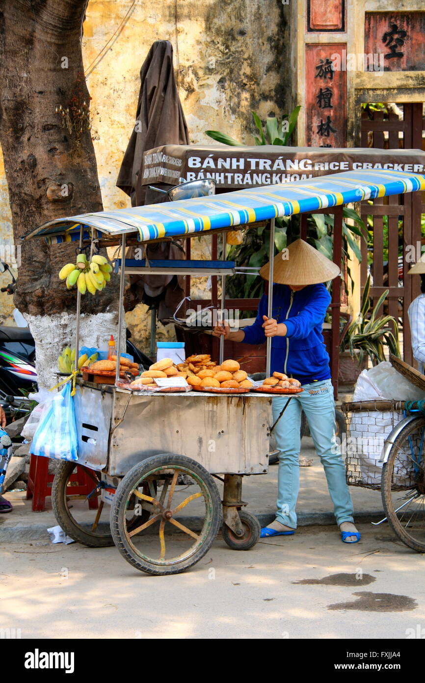 L'alimentation de rue et les fruits vendeur dans Hoi An, Vietnam avec un chariot portant un chapeau conique nón lá, Banque D'Images