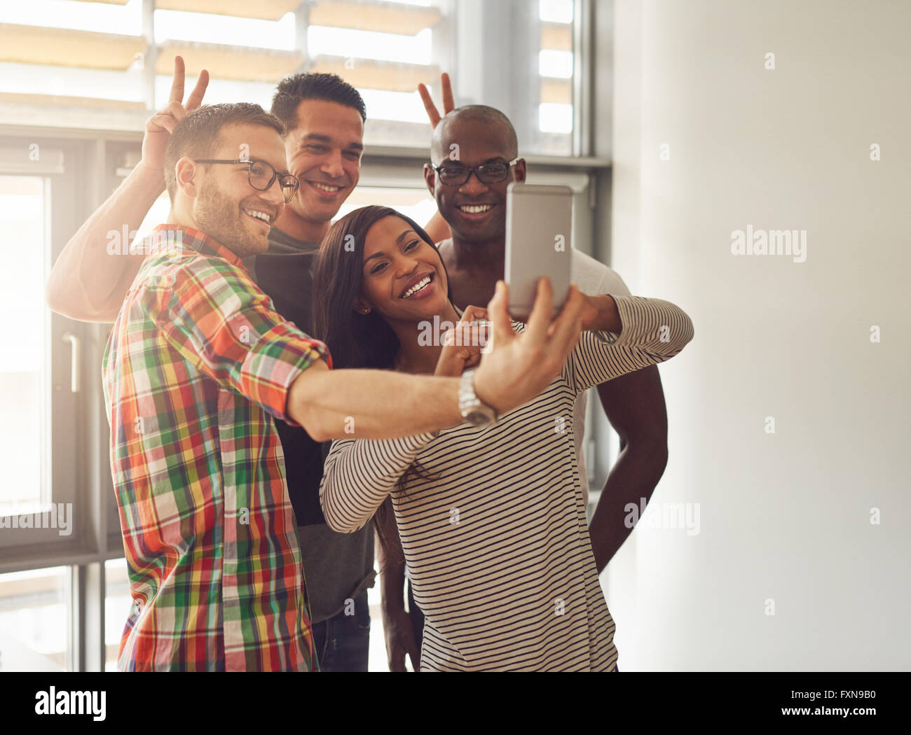 Groupe diversifié de professionnels jeunes travailleurs à prendre des photos et de faire des gestes symboliques pour appareil photo téléphone au petit bureau en face Banque D'Images