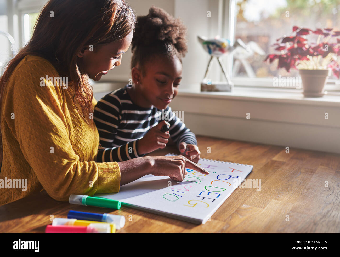 Femme et enfant alphabet d'apprentissage à la maison, mère et fille noire Banque D'Images