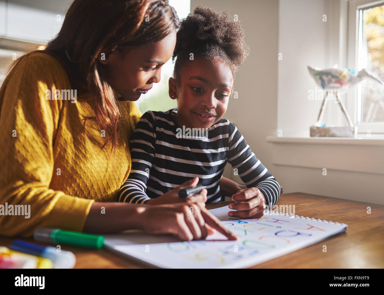 L'apprentissage de la mère noire sa fille l'alphabet à la maison en utilisant des couleurs pour dessiner Banque D'Images