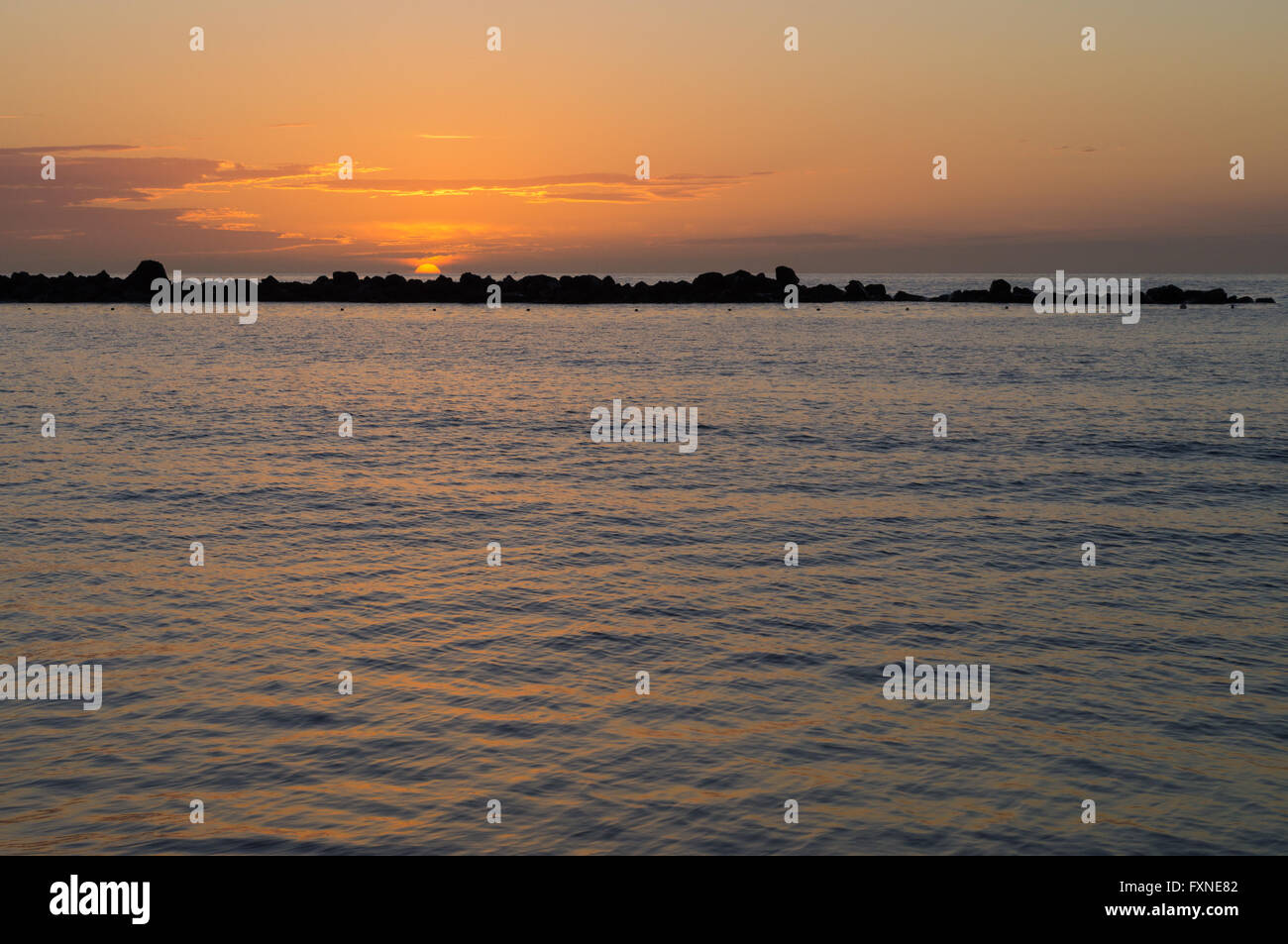 De soleil colorés en océan avec un disjoncteur dans la distance Banque D'Images