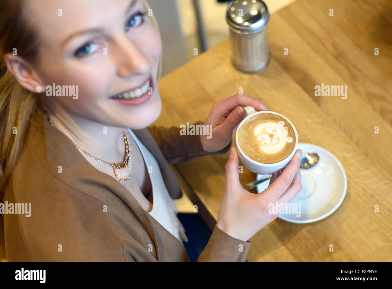 Vue de dessus de smiling blonde femme assise dans un bar avec un cappuccino en face d'elle Banque D'Images