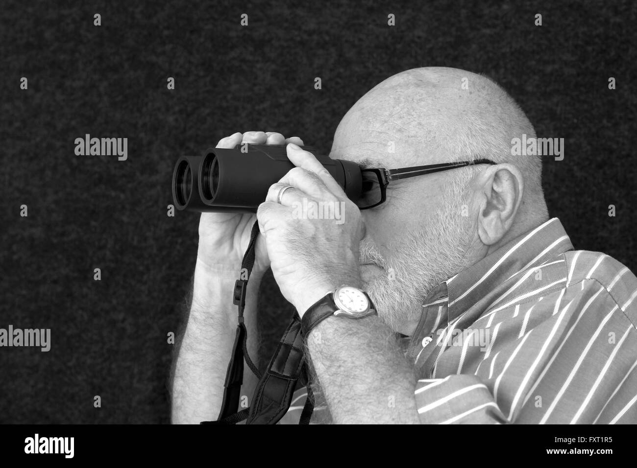 Un vieil homme chauve à la recherche à travers les jumelles. Banque D'Images