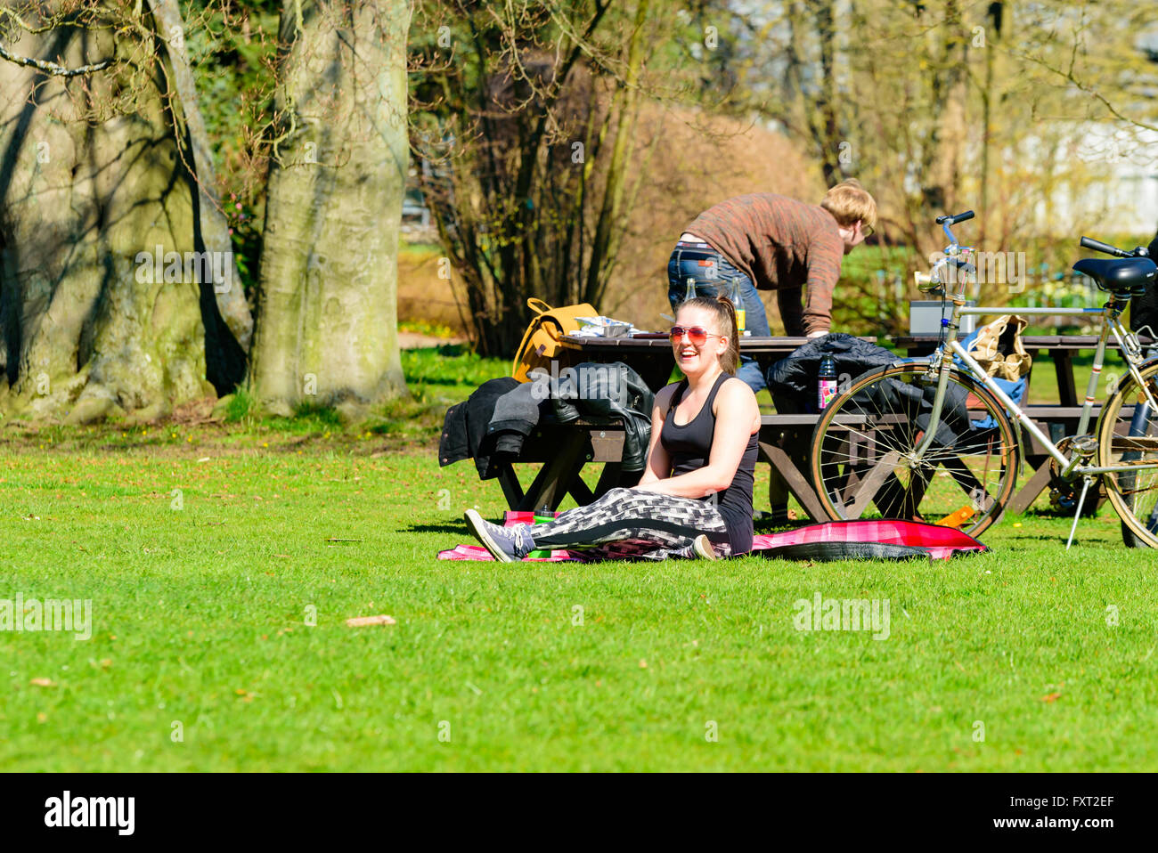 Lund, Suède - 11 Avril 2016 : tous les jours la vie en ville. Jeune femme adulte s'asseoir sur une couverture dans un parc, souriant à l'activité autour d'h Banque D'Images