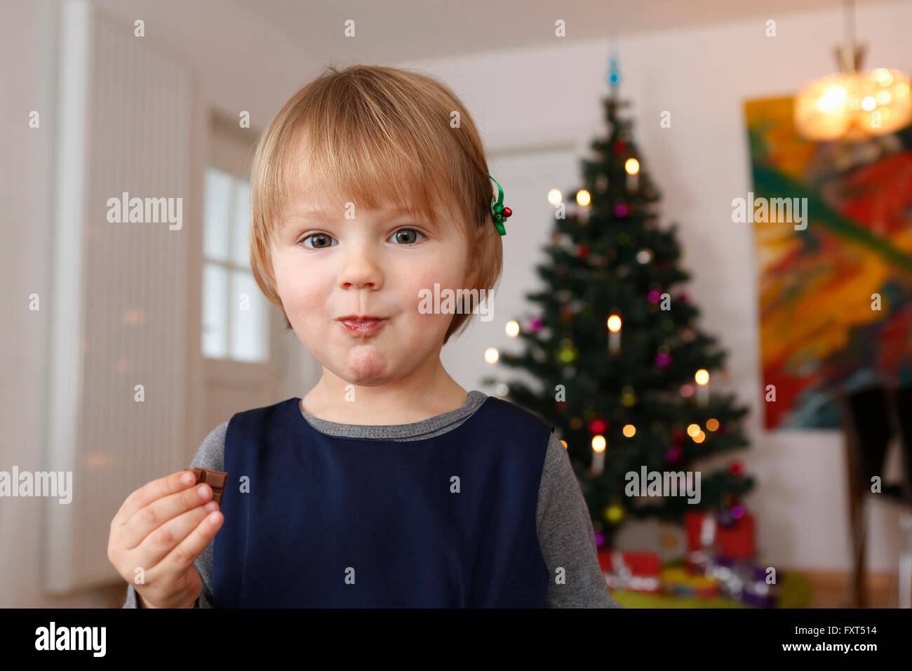 Girl in front of Christmas Tree manger du chocolat looking at camera Banque D'Images