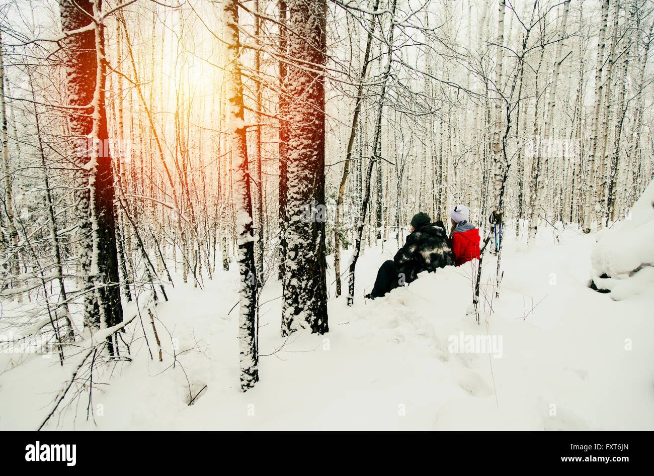 Couple assis dans la forêt enneigée, regardant le coucher du soleil, la Russie Banque D'Images