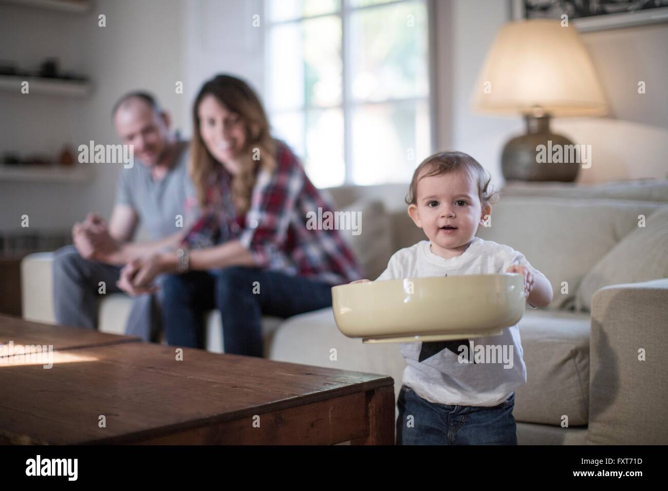 Baby Boy in living room holding grand bol looking at camera smiling Banque D'Images