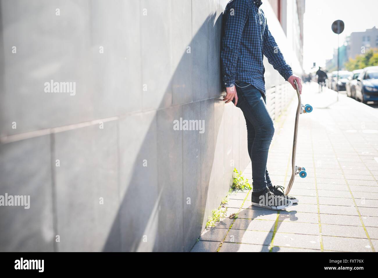 Young male skateboarder urbain appuyé contre la paroi de trottoir Banque D'Images