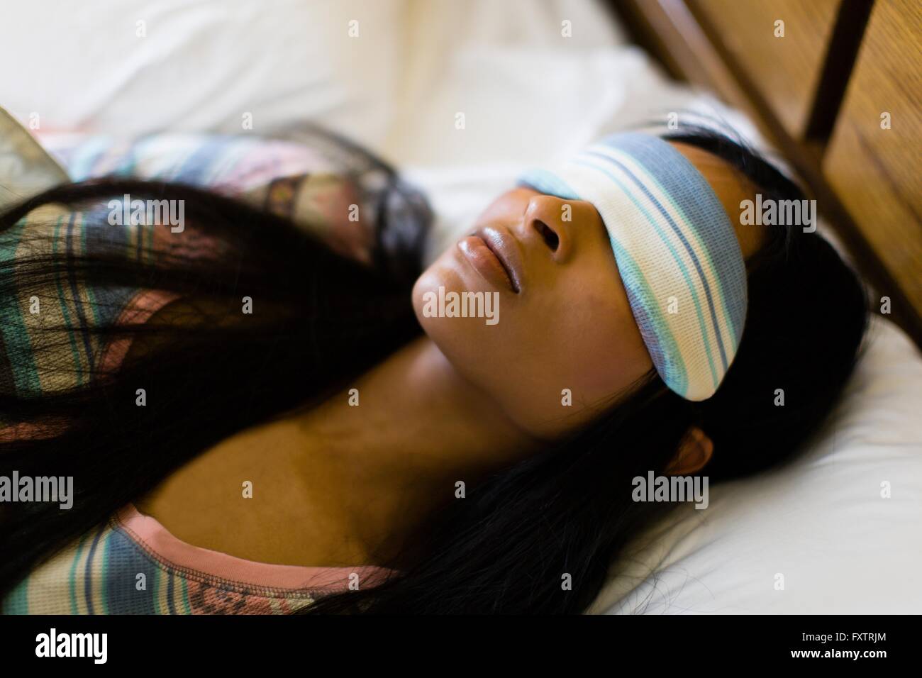 Tête et épaule shot of young woman in bed wearing sleepmask Banque D'Images