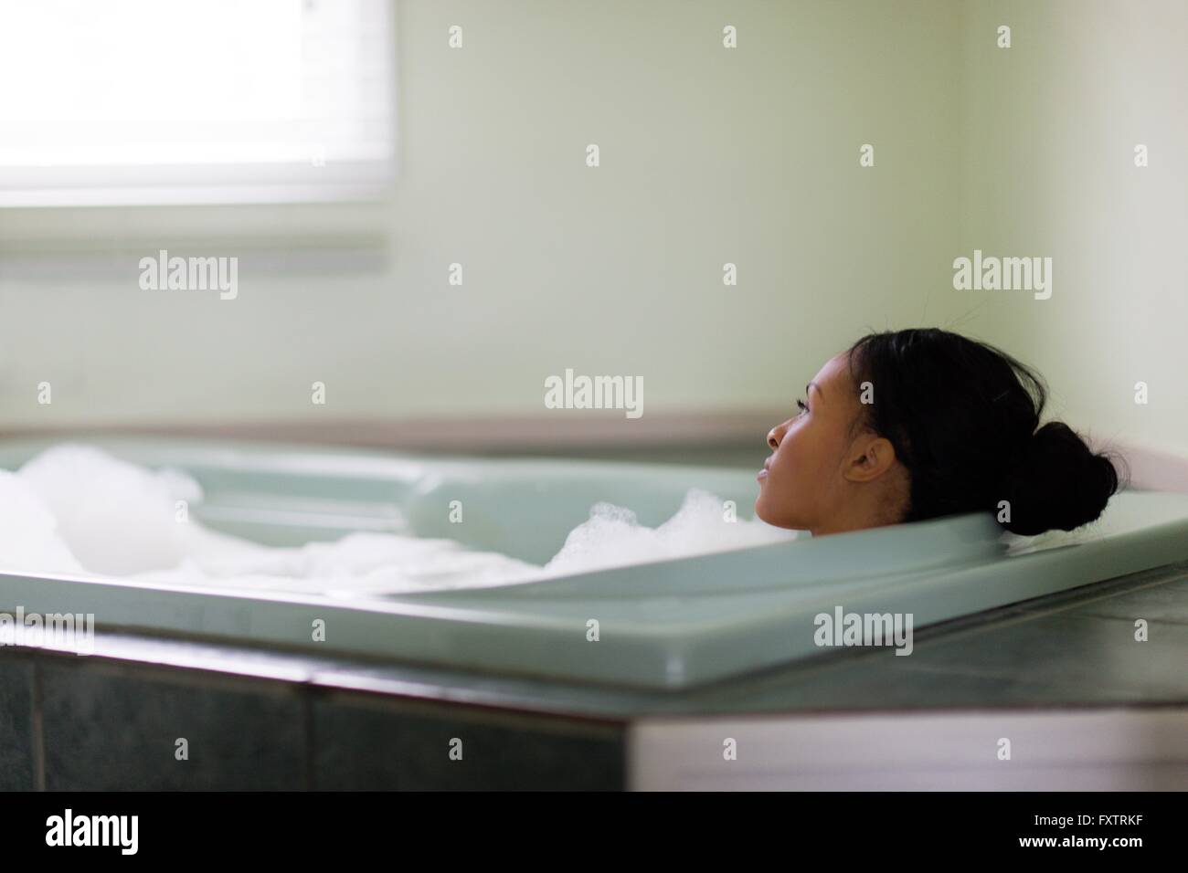 Young woman relaxing in bubble bath le regard à travers la vitre Banque D'Images