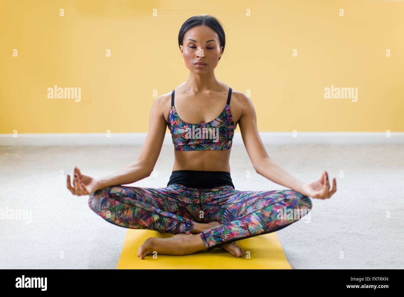 Jeune femme méditant en position du lotus sur un tapis de yoga Banque D'Images