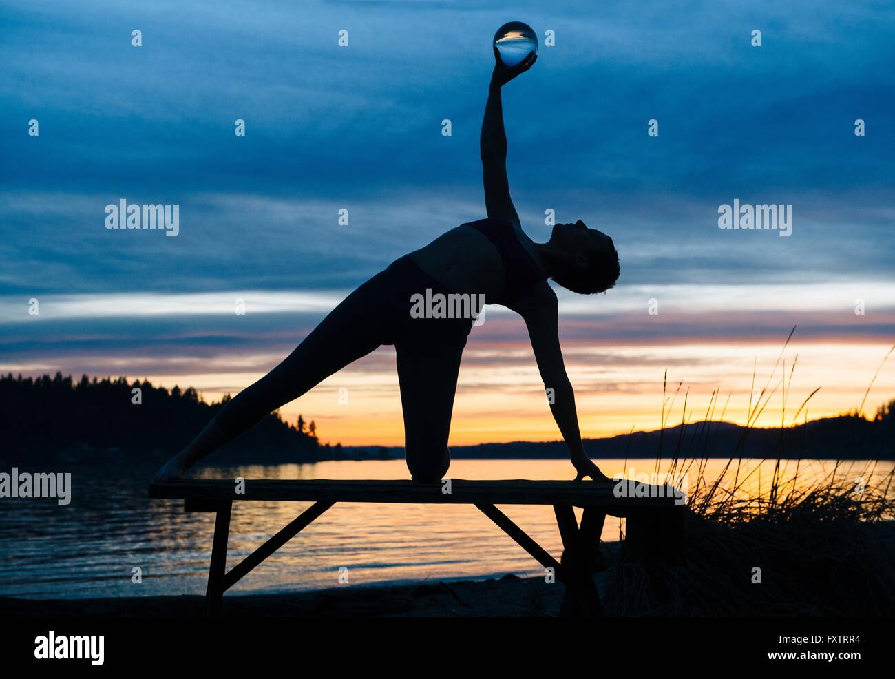 Woman practicing yoga par lac au coucher du soleil Banque D'Images