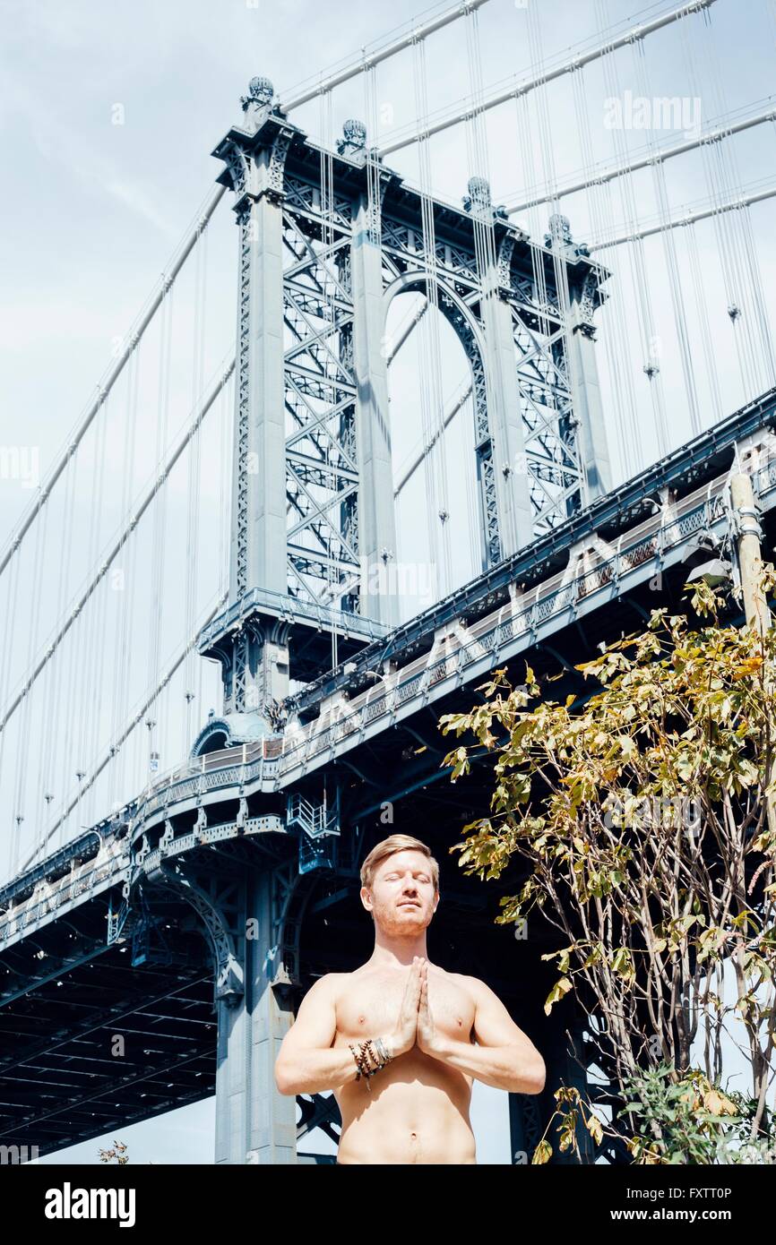 Homme méditant avec mains ensemble en face de pont de Manhattan, New York, USA Banque D'Images