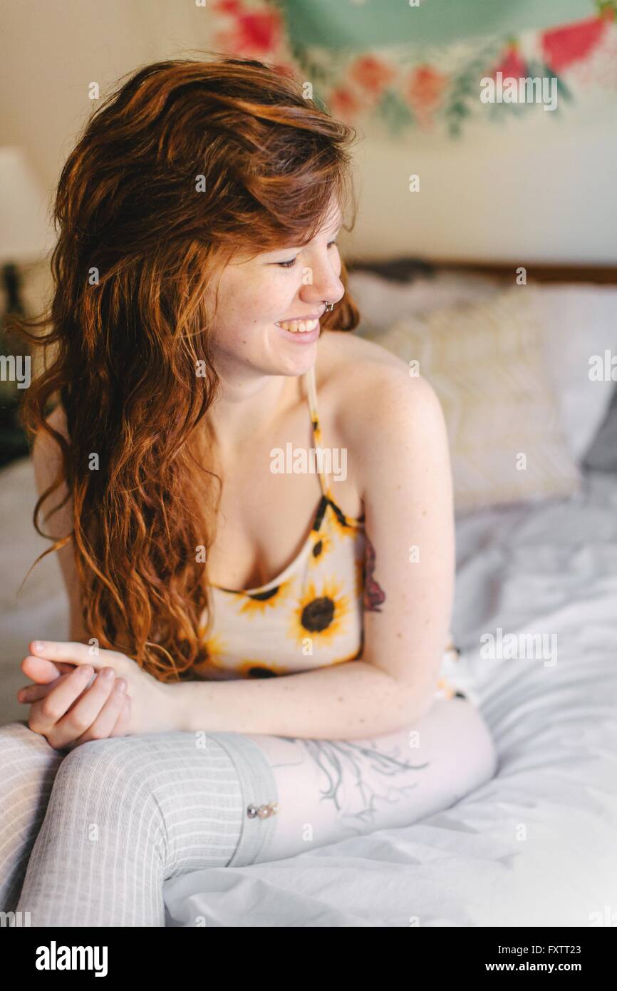 Young woman sitting on bed, smiling Banque D'Images