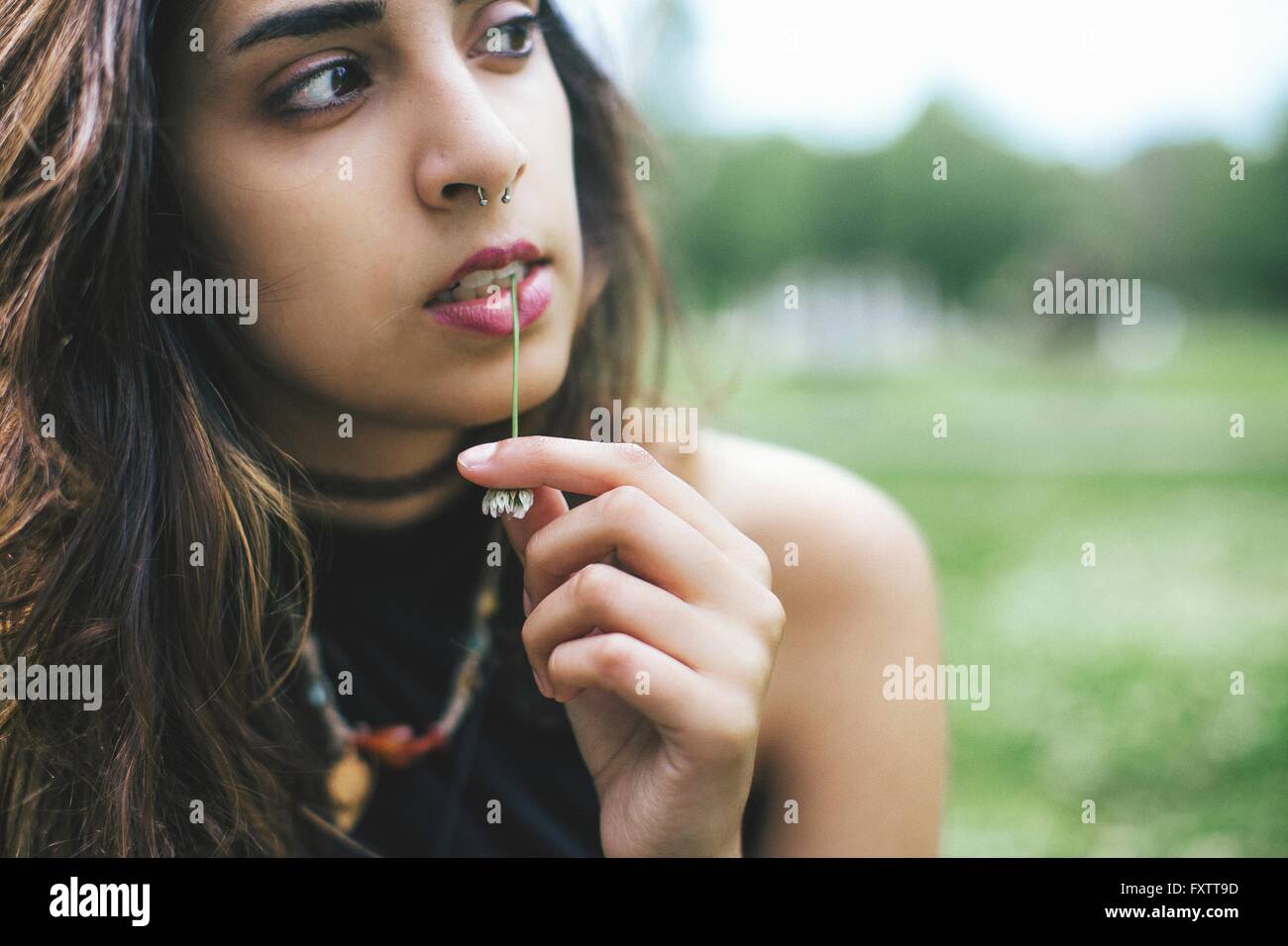 Femme avec anneau dans le nez de mâcher de l'herbe à l'écart Banque D'Images