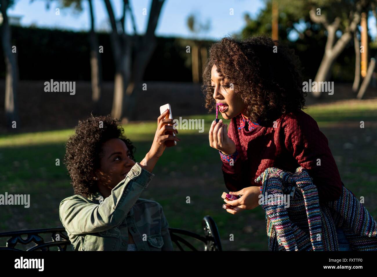 Les amis de park, woman applying Lip Gloss, à la recherche d'un ami dans le smartphone Blackberry Banque D'Images