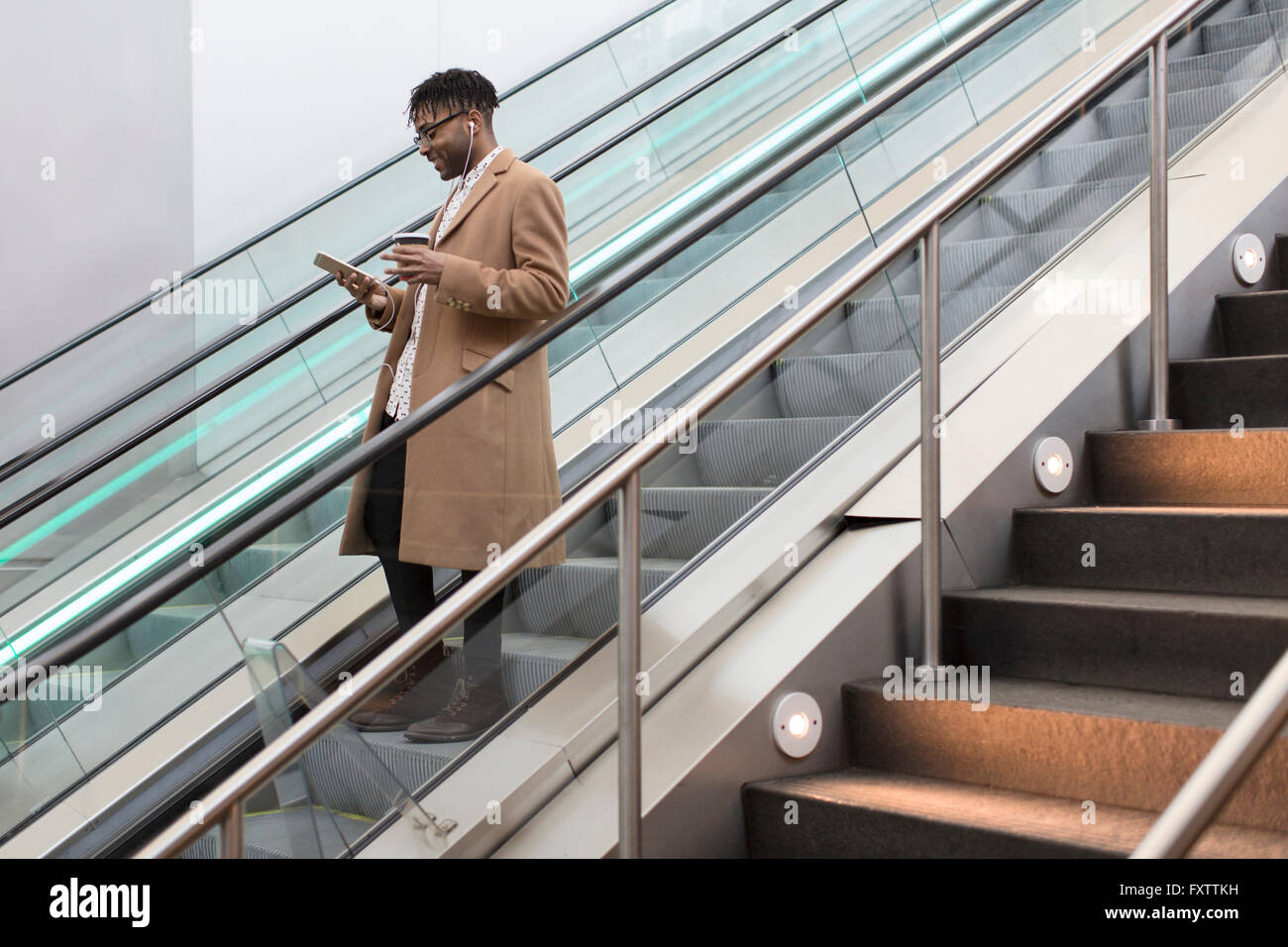 Jeune homme de descendre gare escalator smartphone lecture Banque D'Images