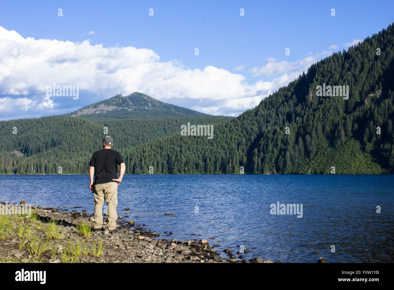 Homme debout et au lac, montagnes et ciel Banque D'Images