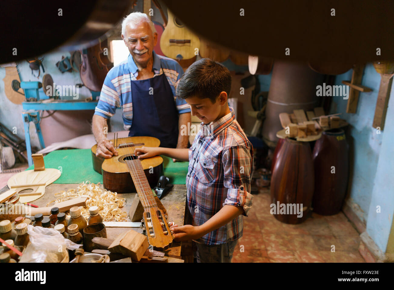 Petite entreprise familiale et traditions : vieux papi avec petit-fils de luthier shop. L'artisan principal enseigne comment accorder une cla Banque D'Images