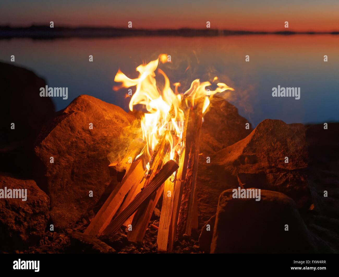 Feu et flammes de feu atmosphérique sur la plage le soir. Encore de l'eau du lac sur le fond avec des couleurs chaudes des soleils Banque D'Images