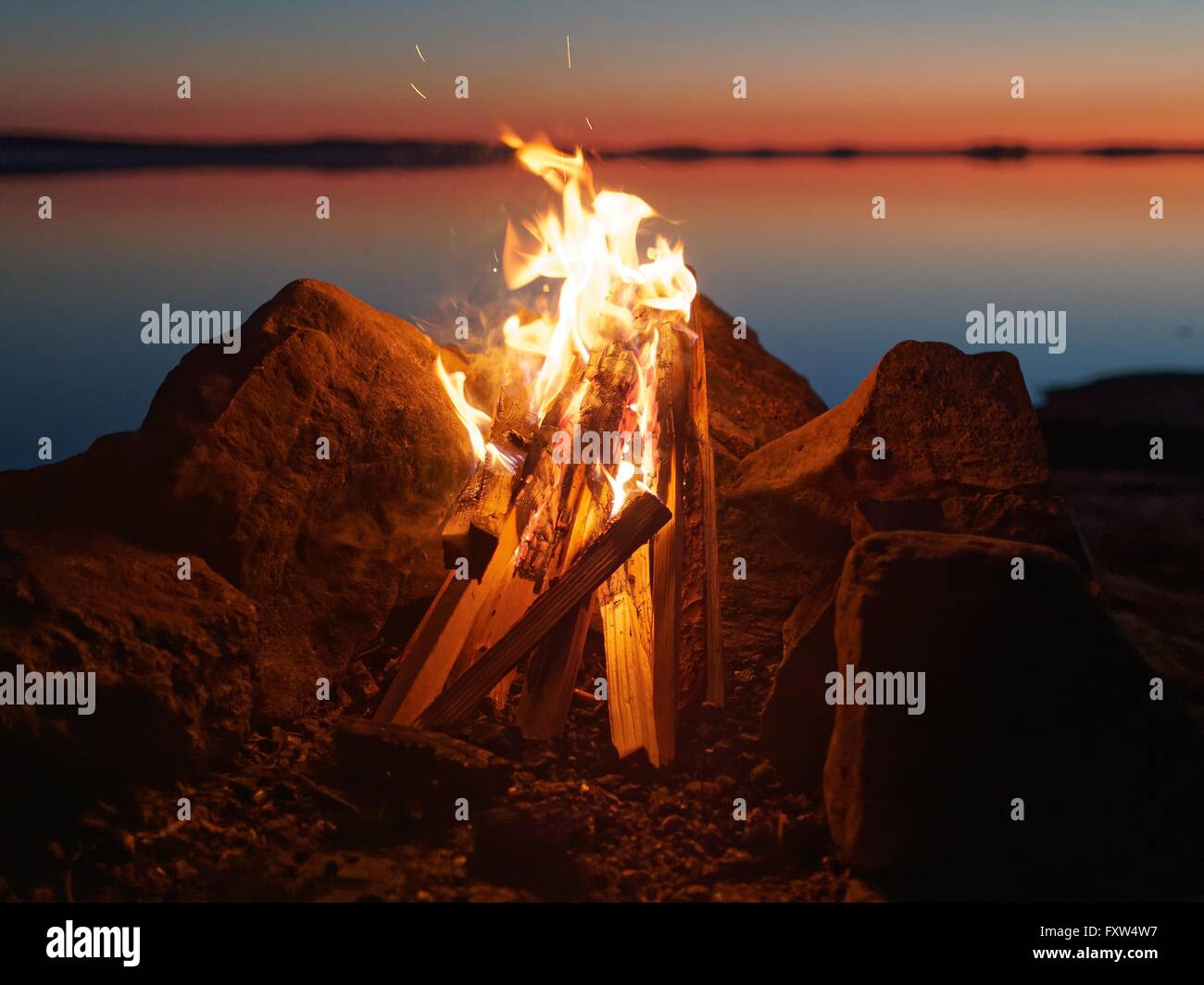 Feu et flammes de feu atmosphérique sur la plage le soir. Encore de l'eau du lac sur le fond avec des couleurs chaudes des soleils Banque D'Images