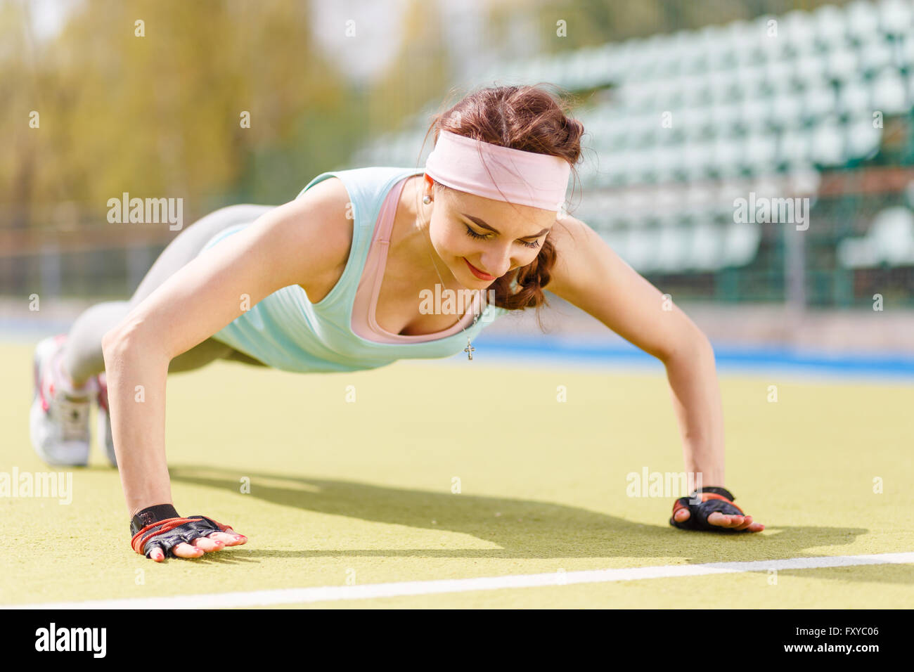 Young woman doing push up de l'exercice à l'extérieur d'entraînement. Smiling girl in sportswear faire formation de remise en forme sur la pelouse Banque D'Images