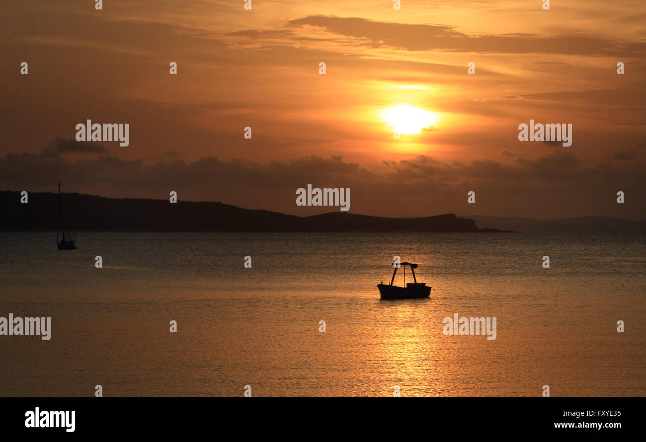 Un bateau ancré dans une baie au coucher du soleil dans les eaux tropicales Banque D'Images