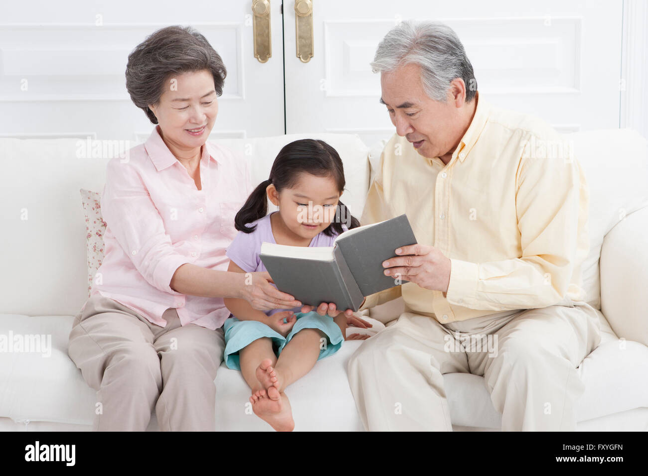 Couple assis sur un canapé et lire un livre à leur petite-fille avec un sourire Banque D'Images