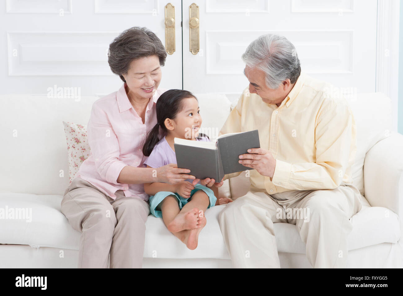 Couple assis sur un canapé et lire un livre à leur petite-fille avec un sourire Banque D'Images