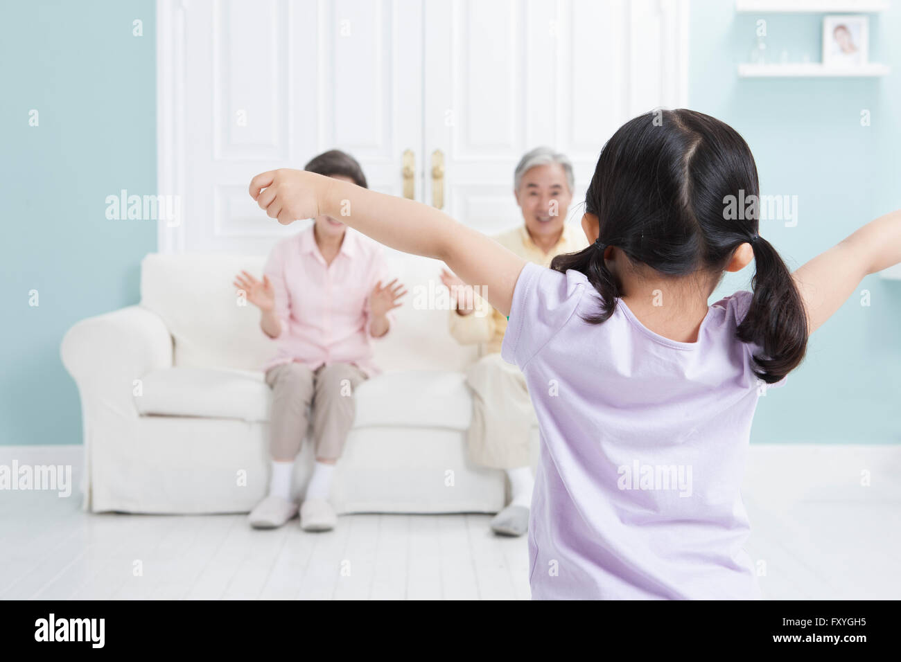 Petite-fille d'ouvrir ses bras large et ses grands-parents, assis sur un canapé et de voir son sourire Banque D'Images