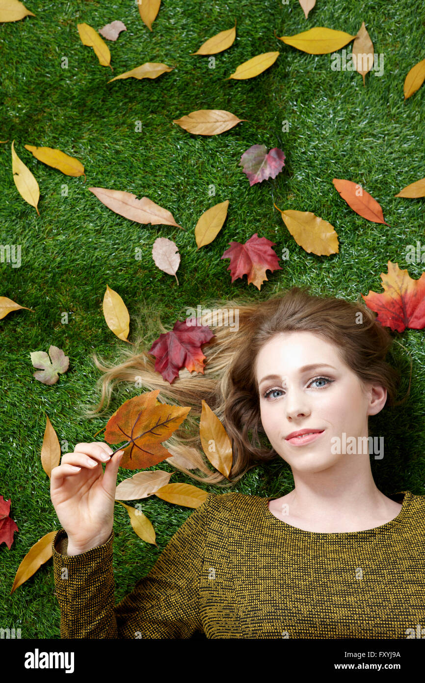 High angle d'une femme couchée sur l'herbe avec les feuilles tombées représentant l'automne Banque D'Images