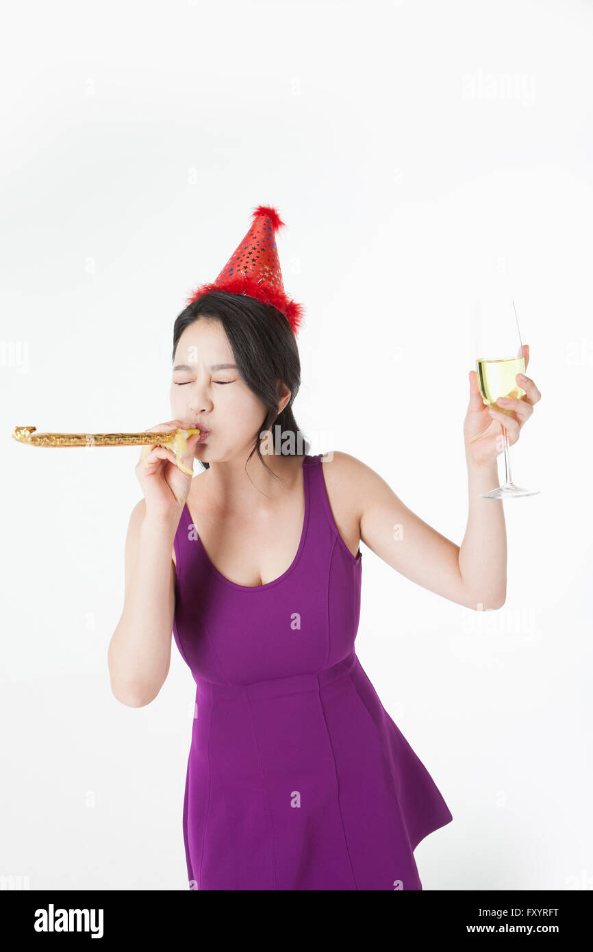 Young woman blowing a party horn tenant un verre de champagne fermer les yeux Banque D'Images