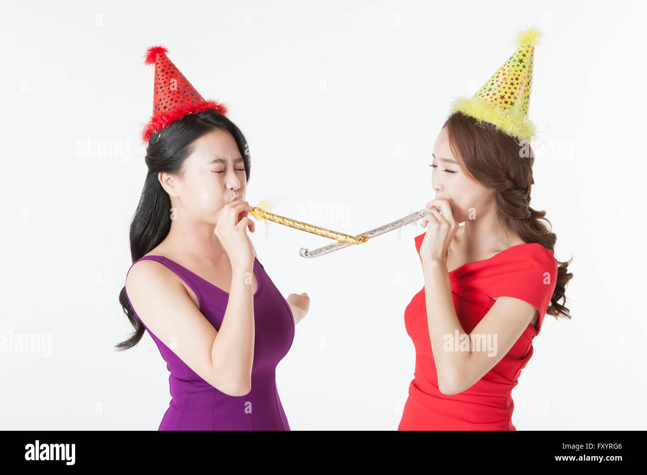 Vue de côté portrait de deux smiling women blowing party horns face à face Banque D'Images