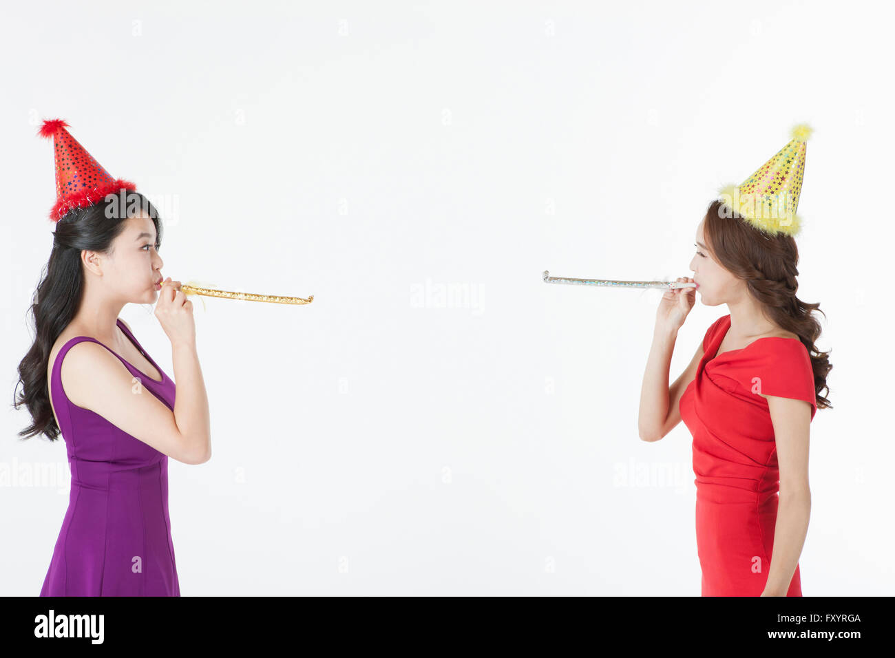 Portrait de deux jeunes smiling women blowing party horns face à face Banque D'Images